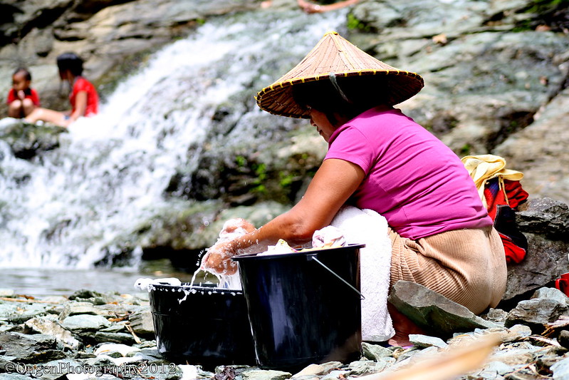 A photo of a woman washing her hands with water in a bucket next to a stream in the Philippines. © 2012 Yujin / Ongen Photography via Flickr