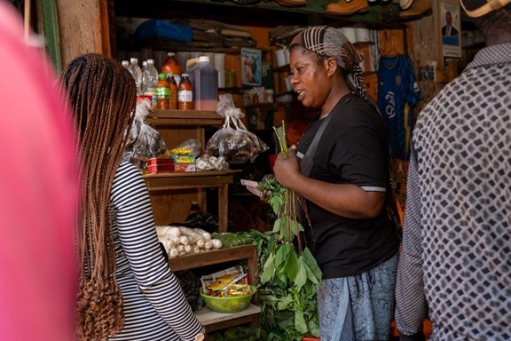     Racheal Chibalama, one of the recipients of the €525 microenterprise grant, is serving a client at her grocery store in Kampala. Chibalama invested her grant to increase the stock of local dishes to cater to her predominantly Congolese customers. PHOTOS BY NATHAN TIBAKU/IRC. 2024.
