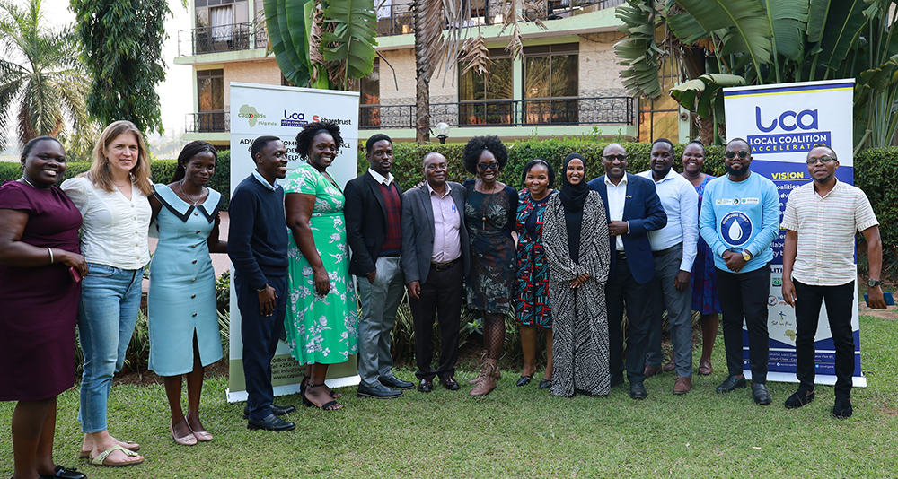 Attendees at an LCA Uganda event stand outdoors on the grass in front of trees