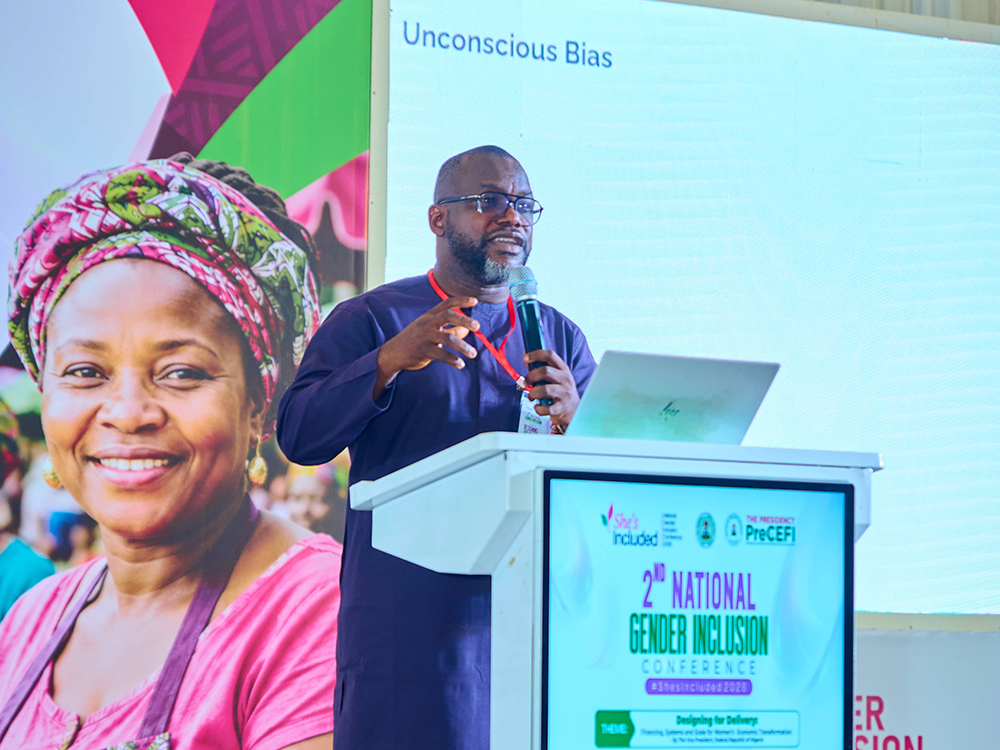 Sam presenting on stage at the event in front of a projector screen showing a slide that says Unconscious Bias at the top
