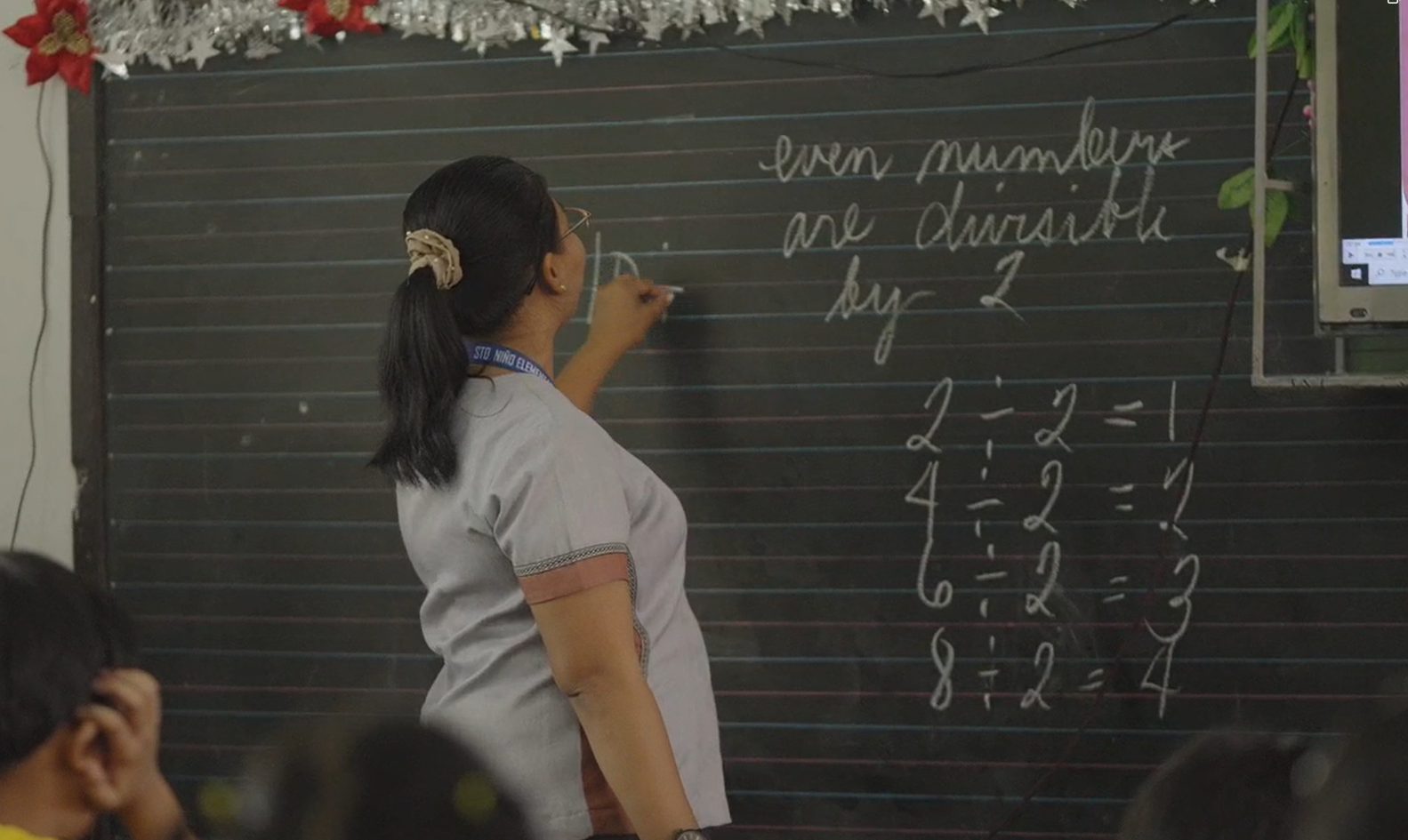 A teacher standing and writing a math lesson on a classroom chalkboard in the Philippines