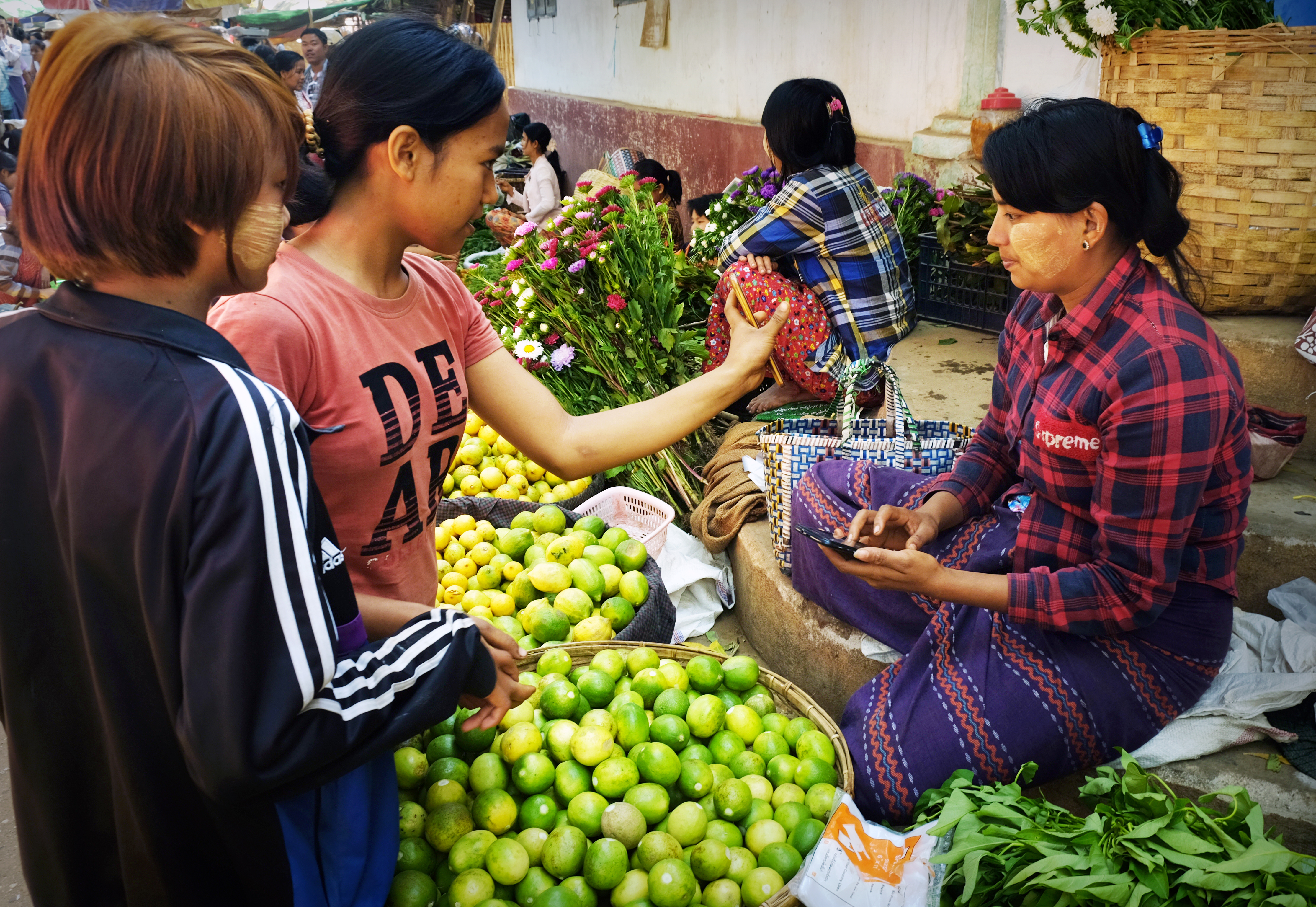Women making a mobile payment at a local vegetable market in Bagan, Myanmar. © 2019 silentwings_M_Ghosh / Shutterstock.com