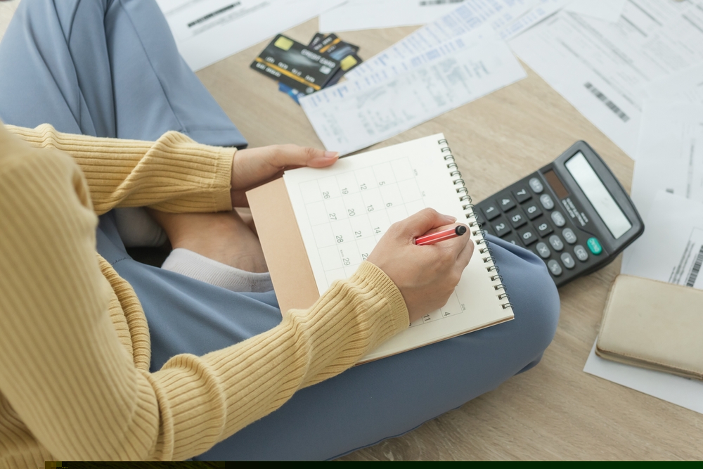 Photo of a woman holding a calendar surrounded by receipts, documents, credit cards, and a calculator.