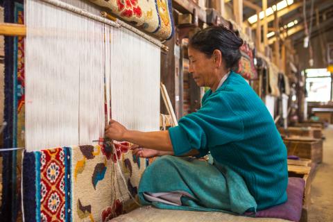 A Tibetan woman works as a weaver in the carpet workshop of the Tibetan Refugee Self-Help Centre in Darjeeling, India. © 2017 Shutterstock / Mazur Travel