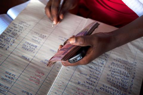 Photo d'une personne écrivant avec un stylo dans un livre de comptabilité tout en tenant de l'argent liquide et un téléphone dans l'autre main. © 2013 Will Boase