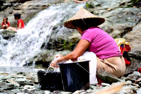 A photo of a woman washing her hands with water in a bucket next to a stream in the Philippines. © 2012 Yujin / Ongen Photography via Flickr