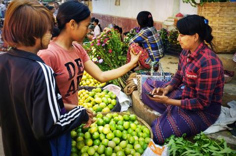 Women making a mobile payment at a local vegetable market in Bagan, Myanmar. © 2019 silentwings_M_Ghosh / Shutterstock.com