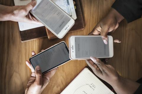 Stock photo of three people sitting in a circle at a table holding their phones to exchange mobile payments