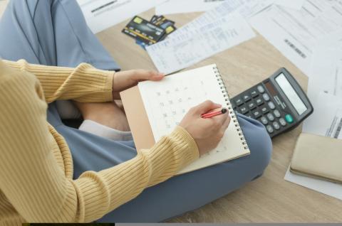 Photo of a woman holding a calendar surrounded by receipts, documents, credit cards, and a calculator.
