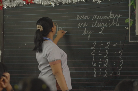 A teacher standing and writing a math lesson on a classroom chalkboard in the Philippines