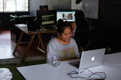 A woman sitting at a desk looking at a laptop screen while smiling