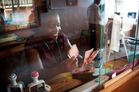 A woman counting bills and smiling while sitting behind the teller window in a bank in Uganda