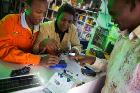 People in Kenya standing at a shop counter examining phones and other electronic products